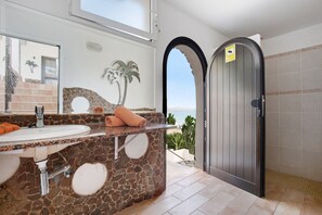 A bathroom with a stone sink, a mirror, and a view of the sea.