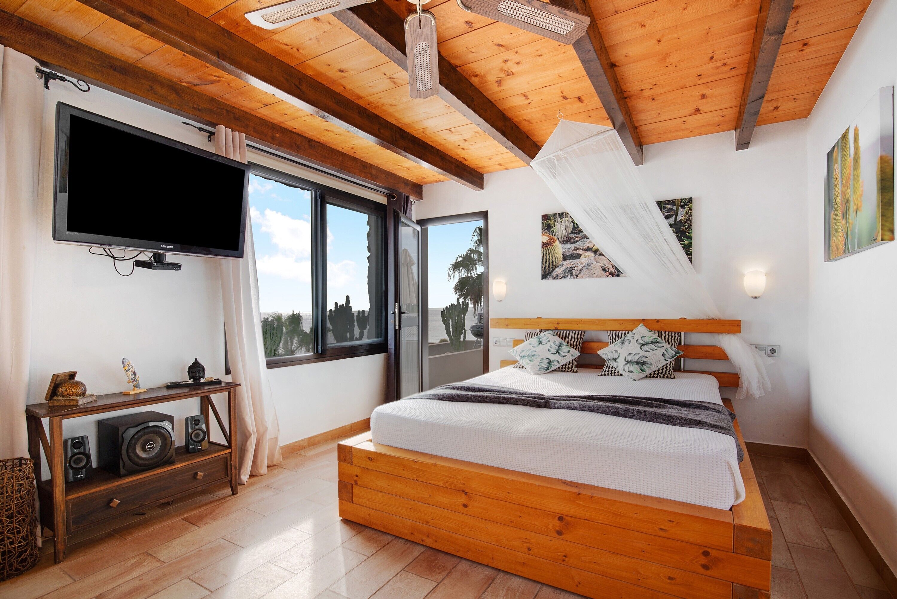 Een slaapkamer met een houten bed, een aan de muur bevestigde televisie en een raam met uitzicht op het landschap.