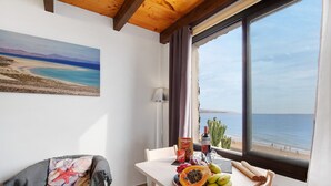 Ein Zimmer mit großem Fenster, Obst auf einem Tisch, einem Stuhl, einem Gemälde und einer Pflanze.
