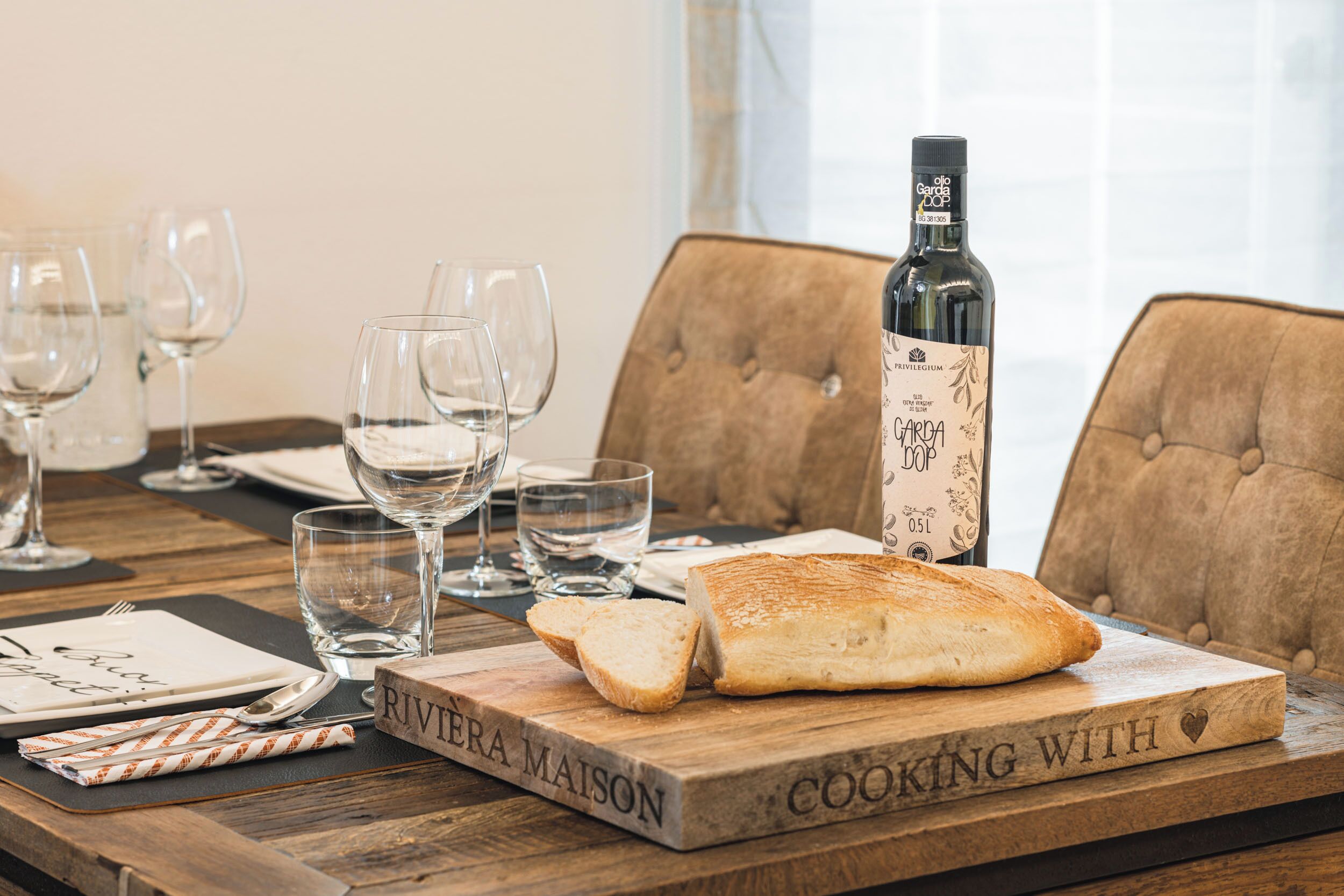 Et træbord med en vinflaske, glas og en friskbagt brød på en skærebræt med teksten "Cooking with".