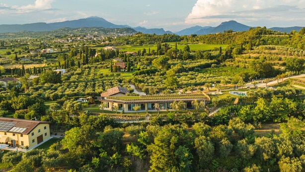 Un vaste domaine dont le bâtiment principal est entouré de jardins luxuriants et de vignobles, avec des montagnes en toile de fond.