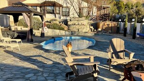 A stone patio with a pool, outdoor furniture, and a wooden deck.