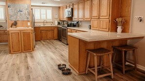 A kitchen with wooden cabinets, a microwave, a stove, and a large island with stools. There are two pet bowls on the floor.