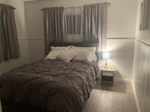 A bedroom with a bed, a nightstand, a lamp, and a window with curtains.