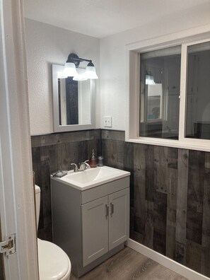 A bathroom with a white sink, a mirror with lights, a toilet, and a window.
