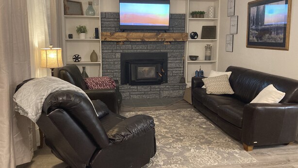 Una sala de estar con chimenea, un televisor montado arriba, un sofá de cuero, un sillón reclinable y una alfombra estampada.