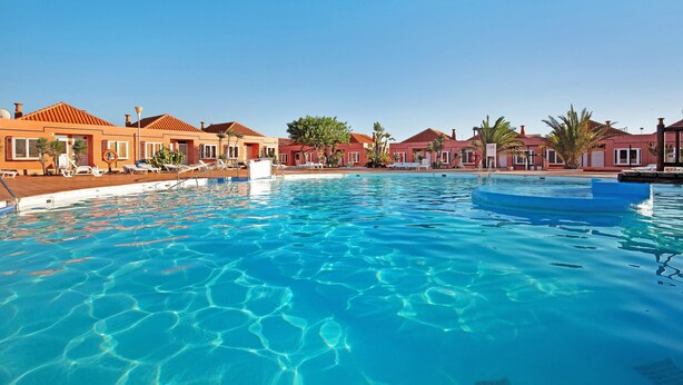 A swimming pool with clear water, surrounded by buildings with red roofs and palm trees. - Holiday Apartment "Paulalucía" with Mountain View, Shared Pool & Wi-Fi (Costa de Antigua)