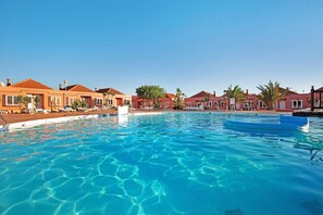 A swimming pool with clear water, surrounded by buildings with red roofs and palm trees. - Holiday Apartment "Paulalucía" with Mountain View, Shared Pool & Wi-Fi (Costa de Antigua)