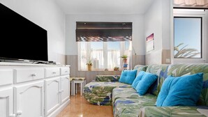 A living room with a flat-screen TV, a sofa with tropical print, and a window with curtains. - Holiday Apartment "Paulalucía" with Mountain View, Shared Pool & Wi-Fi (Costa de Antigua)