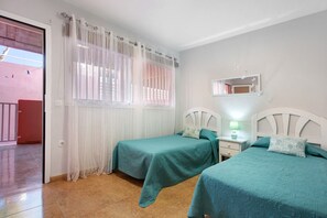 Une chambre avec deux lits, une fenêtre avec des rideaux légers, une table de chevet avec une lampe et un miroir au mur.