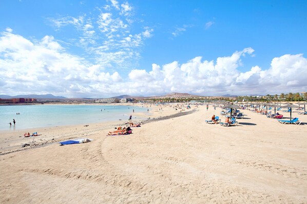 Une plage avec un ciel dégagé, un rivage sablonneux et quelques personnes.