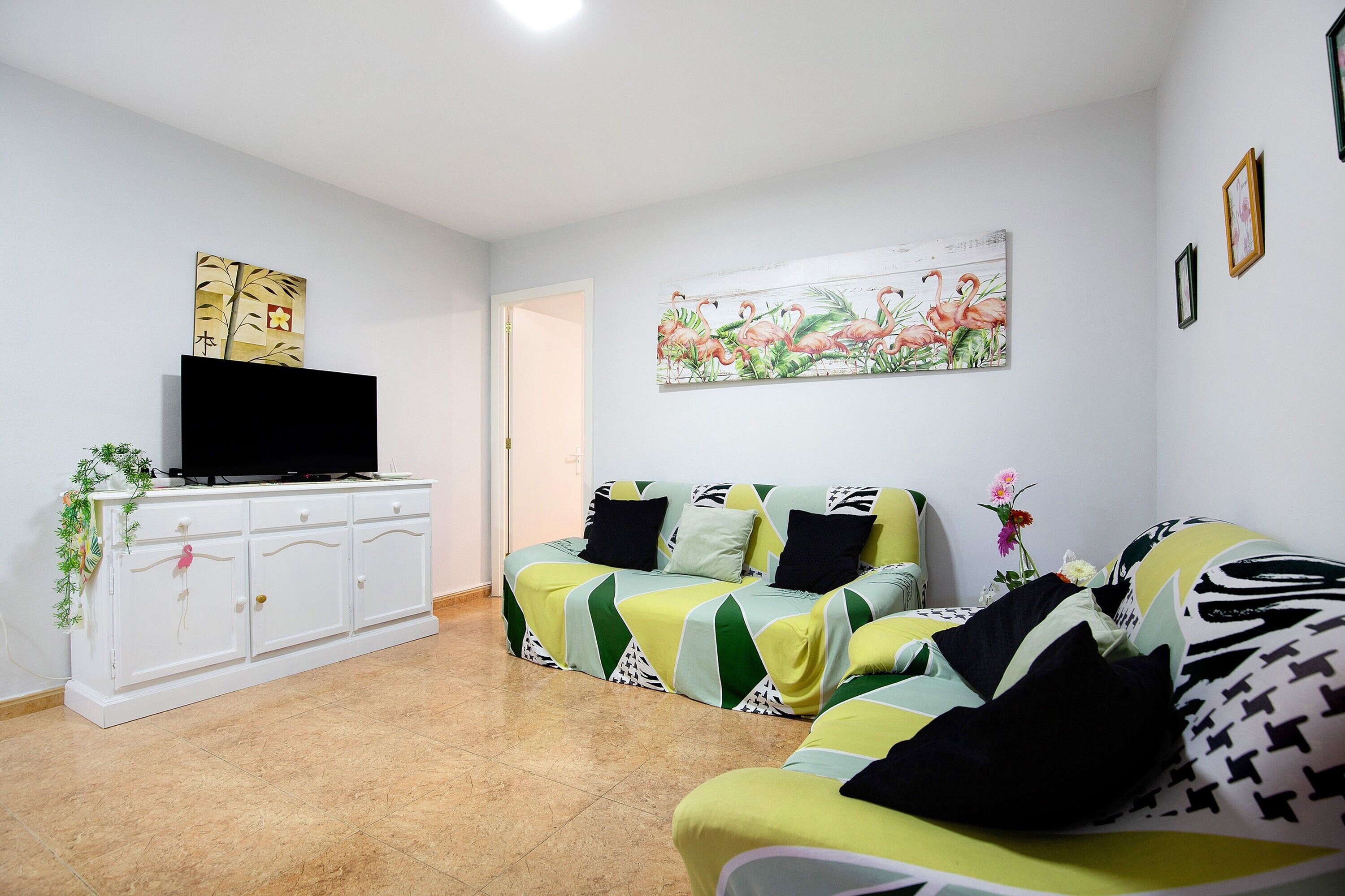 Een woonkamer met een zithoek, een televisie op een kast, en twee schilderijen aan de muur.