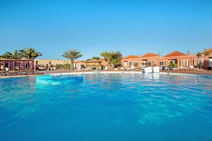 Une piscine à l’eau d’un bleu limpide, entourée de bâtiments aux toits rouges et de palmiers.