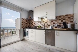 A modern kitchen with a view of the beach, a balcony, and a large window.
