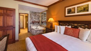 A hotel room with a large bed, a stone wall, a bathroom with a bathtub, and a wooden door.