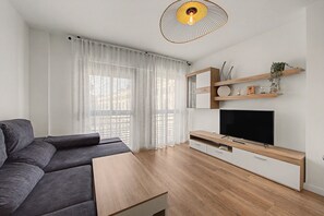 Un salon moderne avec un canapé gris, un meuble TV en bois et un grand téléviseur à écran plat.