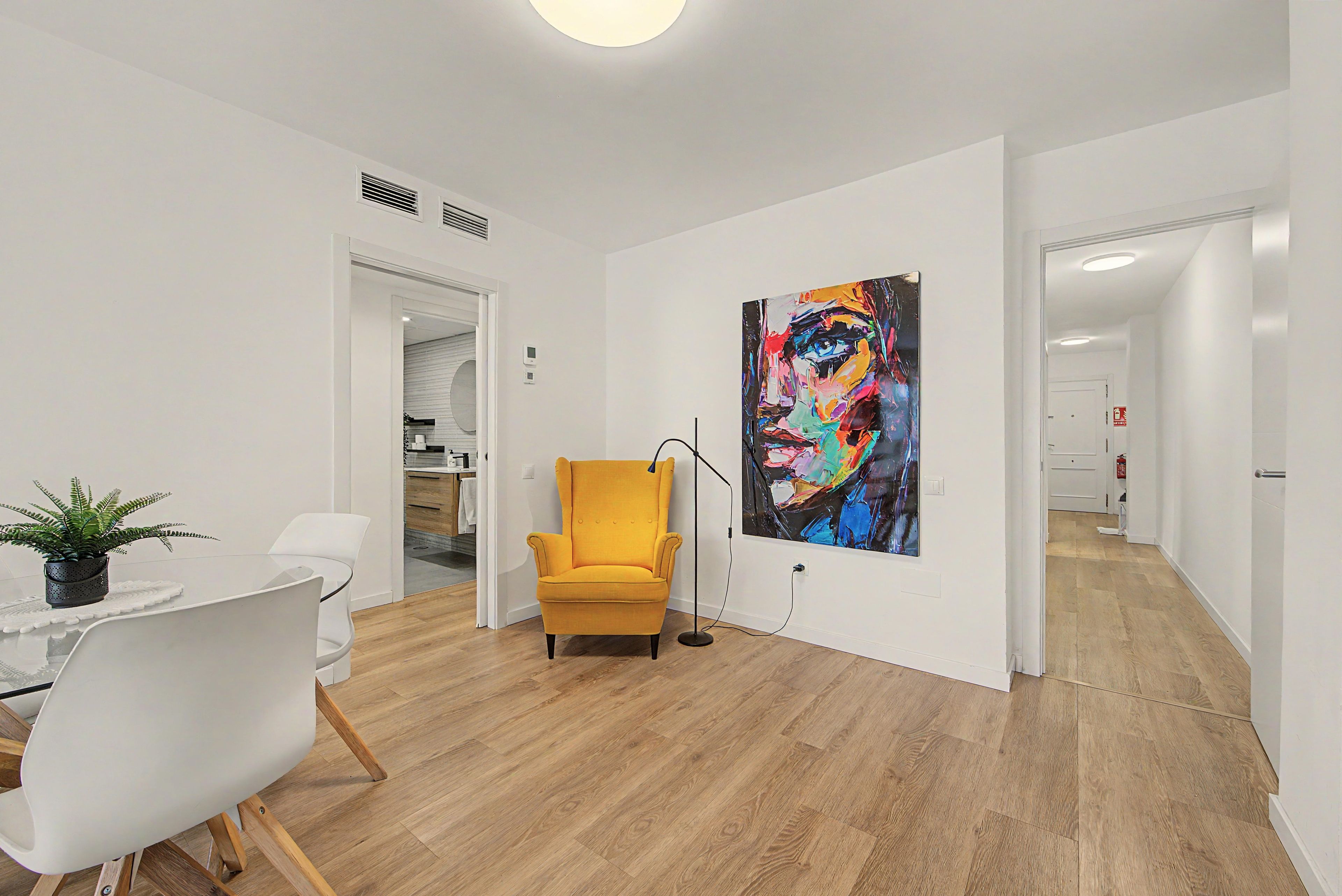 Una sala moderna con comedor, un sillón amarillo y un cuadro abstracto grande en la pared.