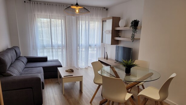Una sala de estar moderna con un sofá, una mesa de comedor de vidrio con sillas, un televisor y una planta.