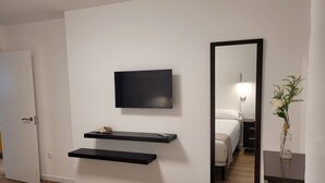 Una habitación de hotel moderna con una televisión de pantalla plana, un espejo y una pequeña repisa.