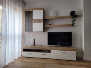 Un salon moderne avec un téléviseur, un meuble en bois et une plante posée sur une étagère.
