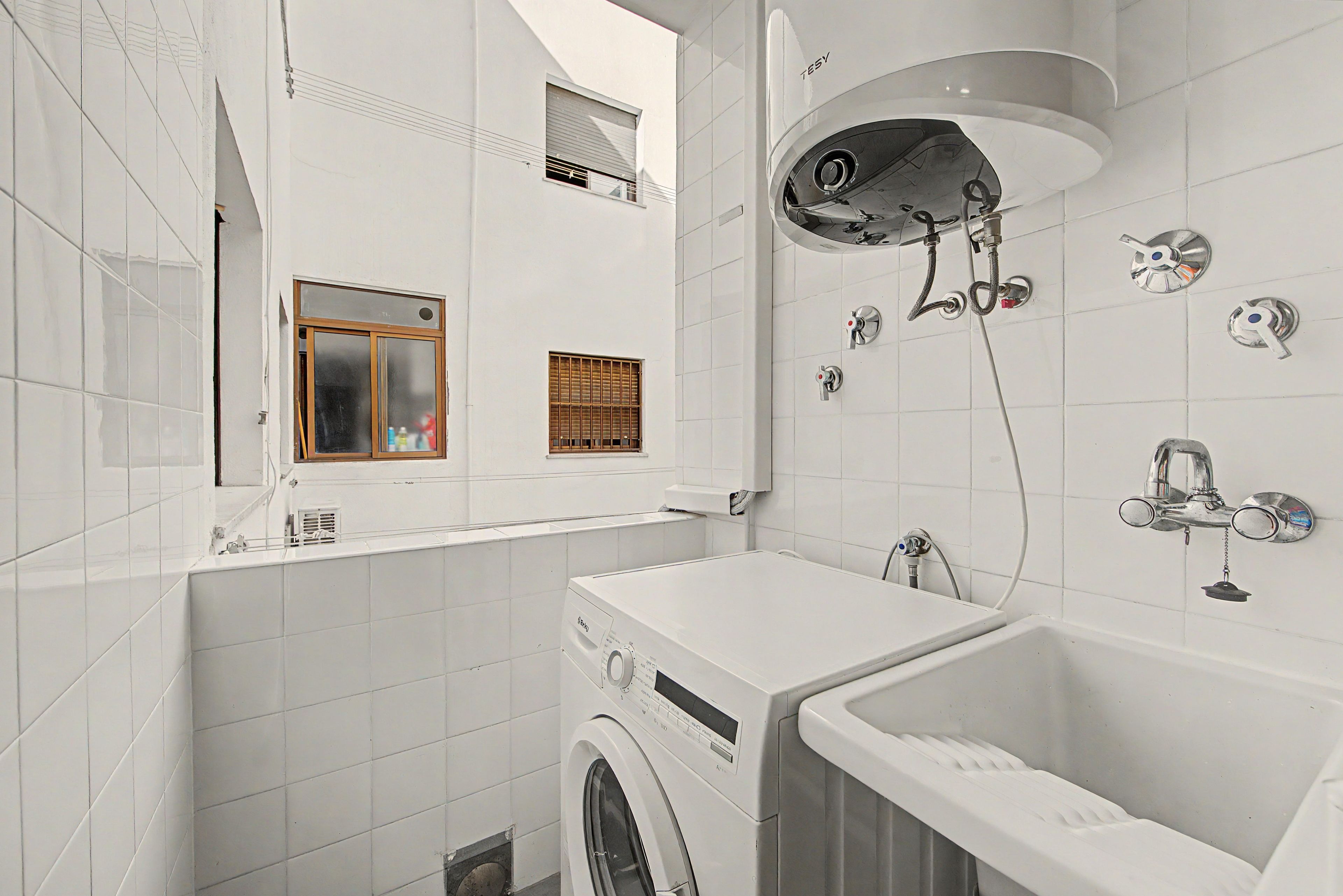Un baño moderno y compacto con lavadora integrada, bañera y ducha con múltiples grifos.
