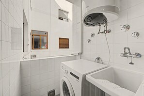 Une salle de bain moderne et compacte, dotée d’un lave-linge intégré, d’une baignoire et d’une douche avec plusieurs robinets.