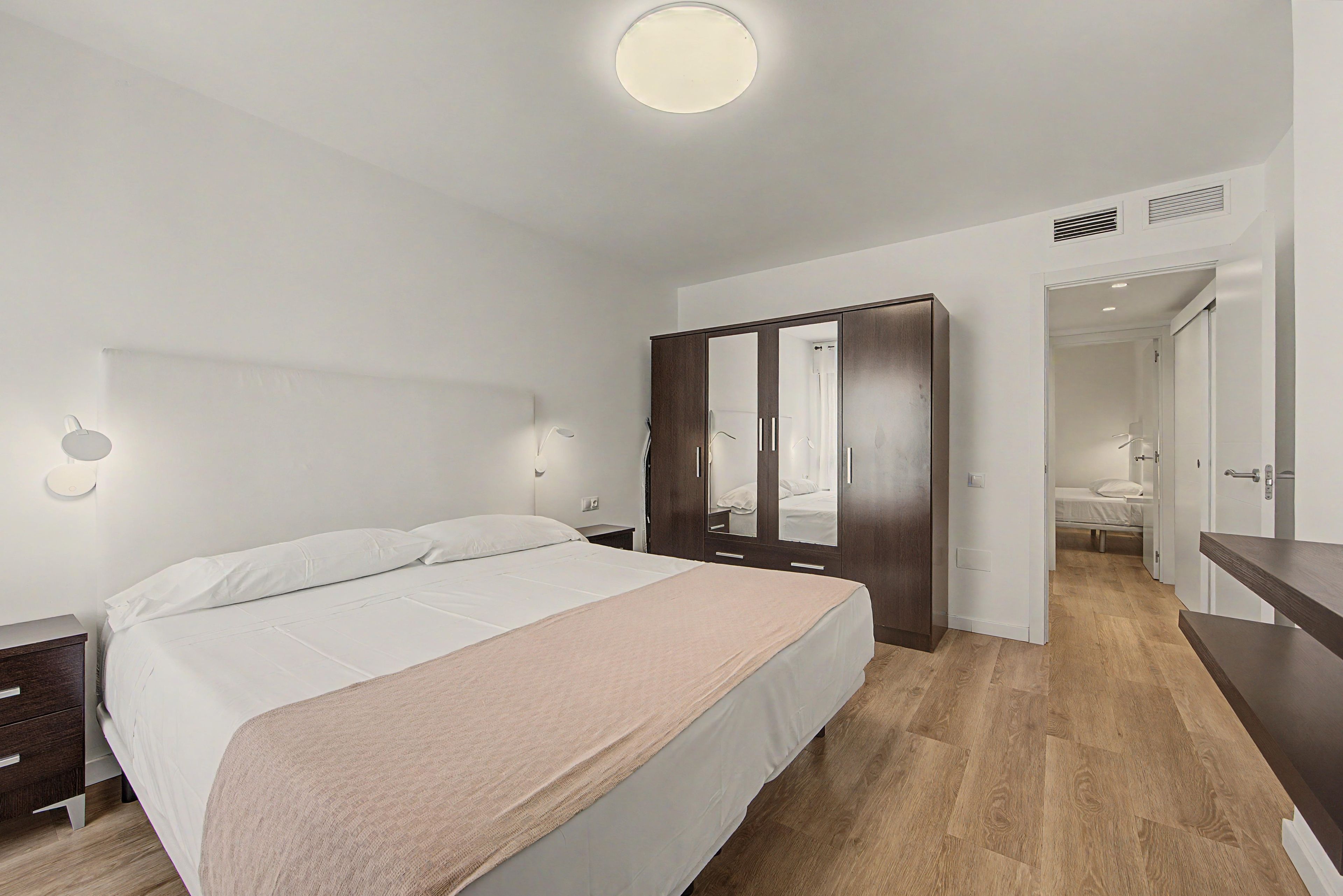 A modern bedroom with a large bed, a wardrobe, and a mirror.