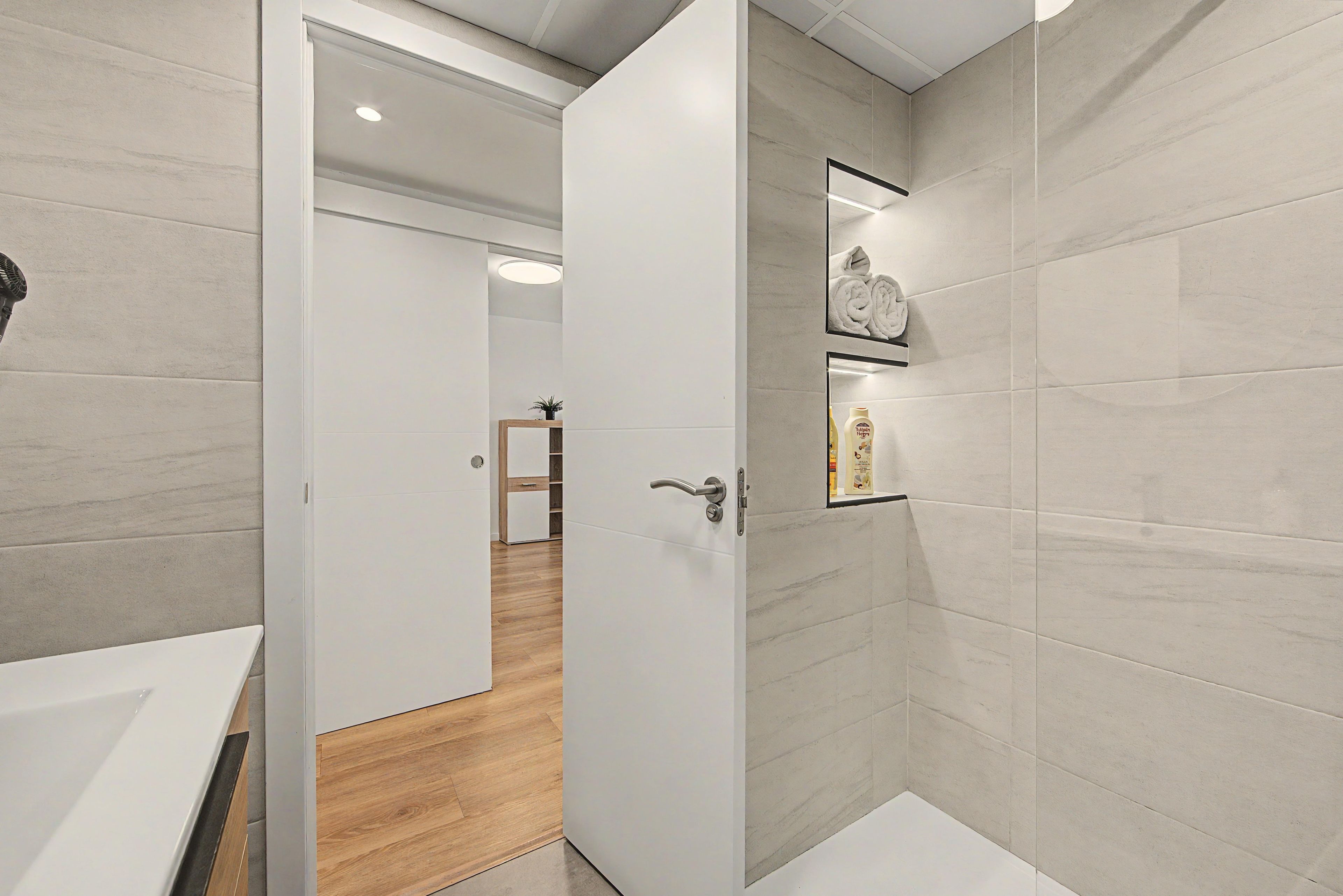 Un baño moderno con un lavamanos blanco, suelo de madera y zona de ducha.