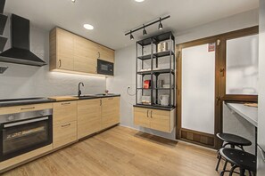 Una cocina moderna con armarios de madera, microondas integrado, horno de acero inoxidable y encimera negra.