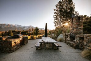 Relax by the stone fireplace in a serene outdoor setting surrounded by lush vegetation and breathtaking mountain views.