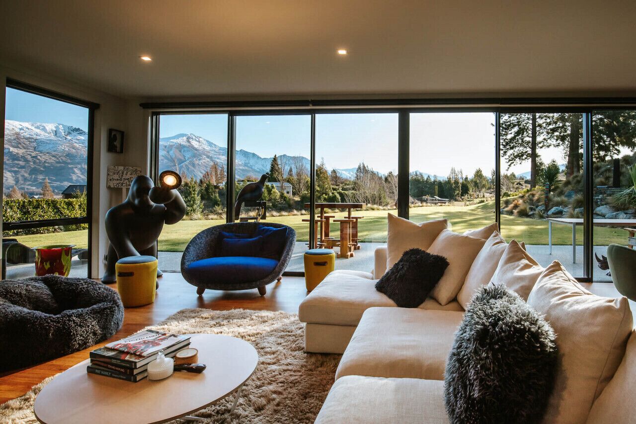 A modern living room with a large window offering a mountain view, a cozy seating area, and a small table with books.