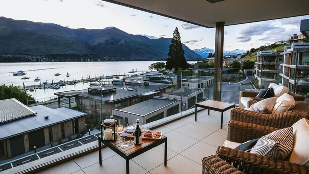 Una terraza con vistas a un lago y montañas, amueblada con sillones de mimbre y una mesa con comida y bebidas.