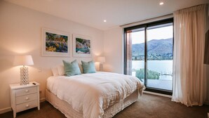 Un dormitorio con una cama grande, dos mesitas de noche y una ventana con vistas a un lago y montañas.