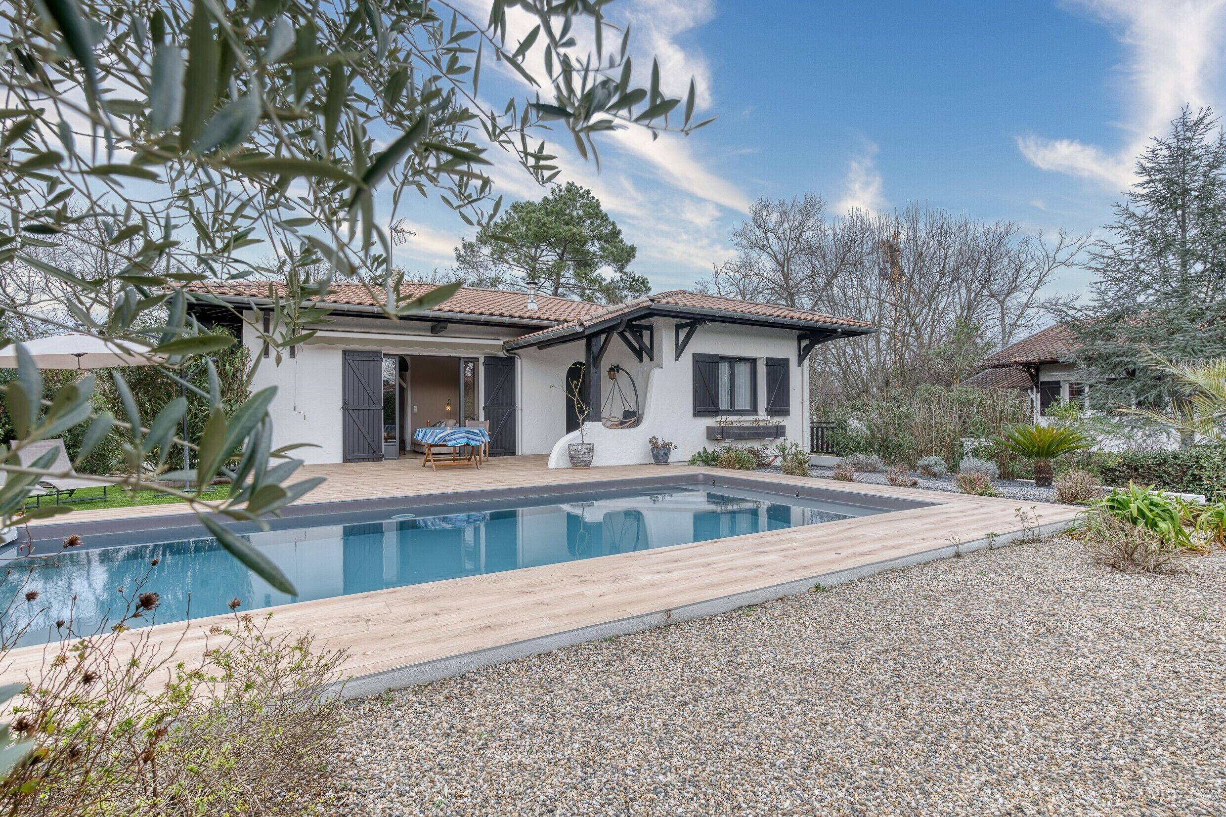 Uma casa moderna com piscina, um pátio com mobiliário de exterior e um jardim com diversas plantas.