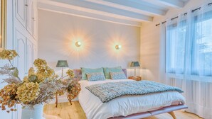 A bedroom with a bed, bedside lamps, a vase with flowers, and a window with curtains. - 4-Star Villa Arcachon – Heated Pool, Garden & Petanque, Sleeps 8 (La Teste-de-Buch)