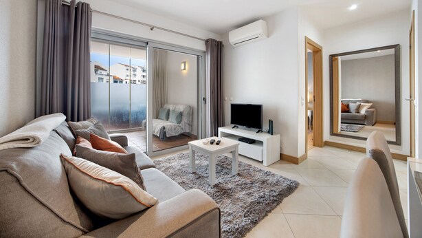 Un salon moderne comprenant un canapé, une table basse, un téléviseur à écran plat et une porte-fenêtre coulissante donnant sur un balcon.