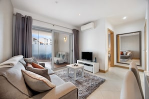 A modern living room with a sofa, a coffee table, a flat-screen TV, and a sliding glass door leading to a balcony.