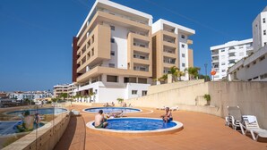 Un bâtiment moderne doté de nombreux balcons, d’une piscine et de chaises longues.