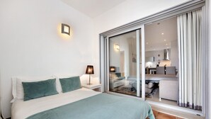 Une chambre à coucher comprenant un lit, une table de chevet, une lampe et une porte-fenêtre coulissante donnant sur un espace de vie.