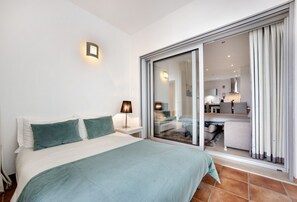 A bedroom with a bed, nightstand, lamp, and a sliding glass door leading to a living area.