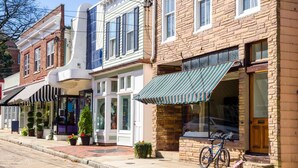 A row of brick buildings with storefronts, a bicycle parked outside, and a sidewalk. - Steps to USNA Gate 3, On-Site Parking & Private Patio at Historic Gatehouse (Annapolis)