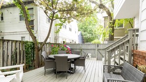 A deck with a round table and chairs, surrounded by a wooden fence and trees. - Steps to USNA Gate 3, On-Site Parking & Private Patio at Historic Gatehouse (Annapolis)