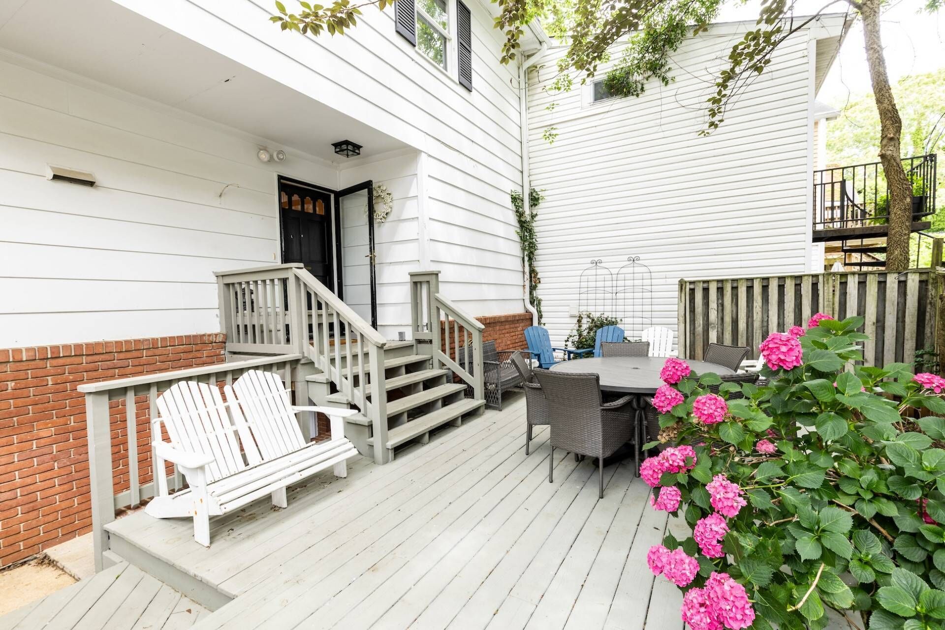 A covered patio with a wooden deck, a round table, and chairs. There is a brick wall and a wooden fence.