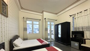 Une chambre d’hôtel avec un lit, une armoire, un bureau avec un ordinateur et une vue sur la ville par la fenêtre.