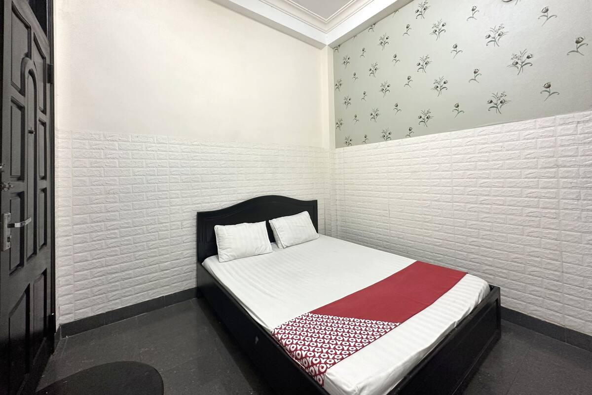 Ein Einzelbett in einem Zimmer mit weißen Backsteinwänden, floralem Wandpapier an einer Wand und einer Tür links.