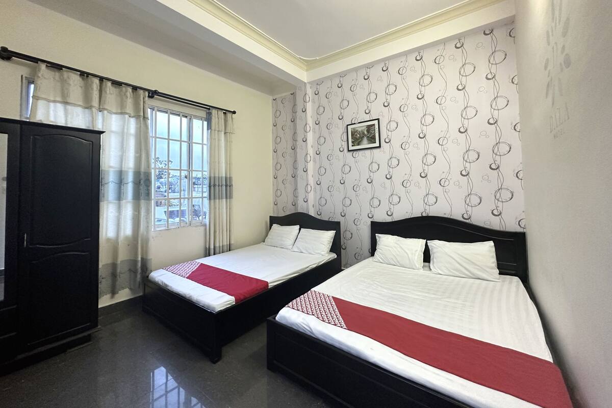 Ein Hotelzimmer mit zwei Einzelbetten, einem Kleiderschrank, einem Fenster mit Vorhängen und einem gemusterten Wandpapier.