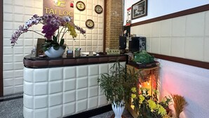 Un comptoir d’accueil avec une pancarte indiquant « TÀI LÒC », des horloges, un ordinateur et une plante en pot.