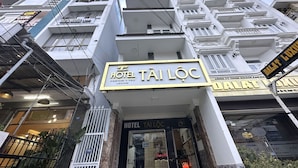 L’entrée d’un hôtel, avec une enseigne indiquant « HÔTEL TAILÒC » et une adresse clairement visible.