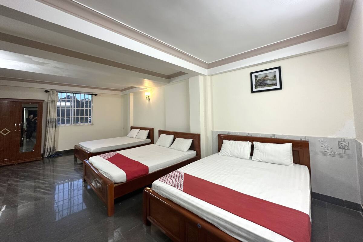 Ein Hotelzimmer mit zwei hölzernen Betten, einem Spiegel, einem Fenster mit Vorhängen und einem gerahmten Bild an der Wand.