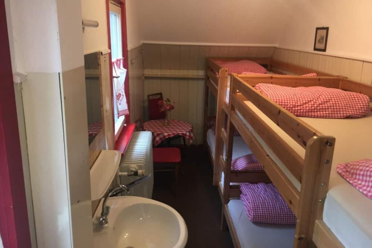 Una habitación pequeña y funcional con literas, un lavamanos y una mesa cubierta con mantel a cuadros rojo y blanco.